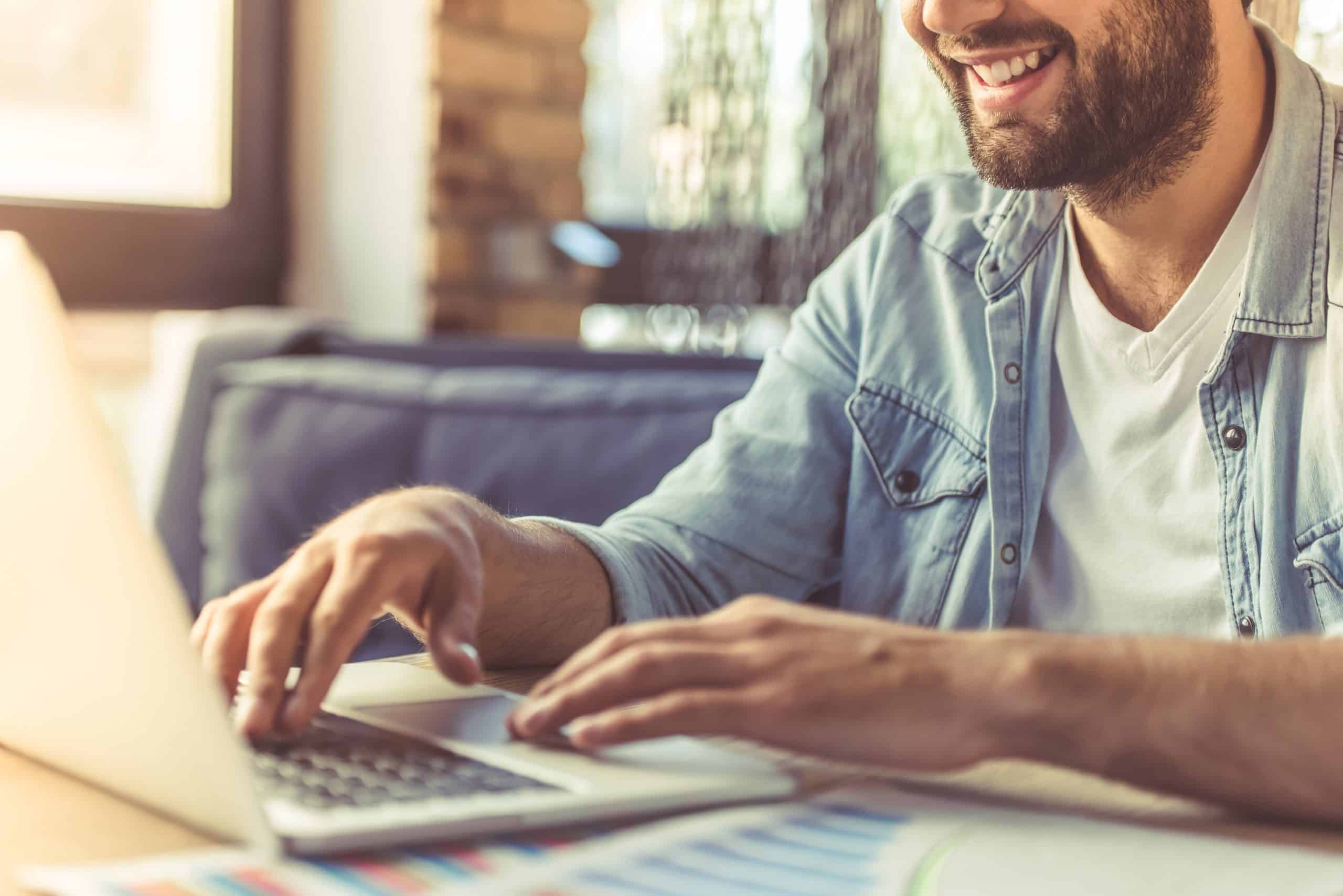 Cropped image of handsome businessman in casual wear using a laptop and smiling while working in the office