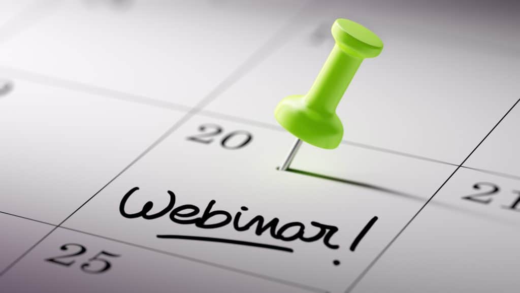 Concept image of a Calendar with a green push pin. Closeup shot of a thumbtack attached. The words Webinar written on a white notebook to remind you an important appointment.